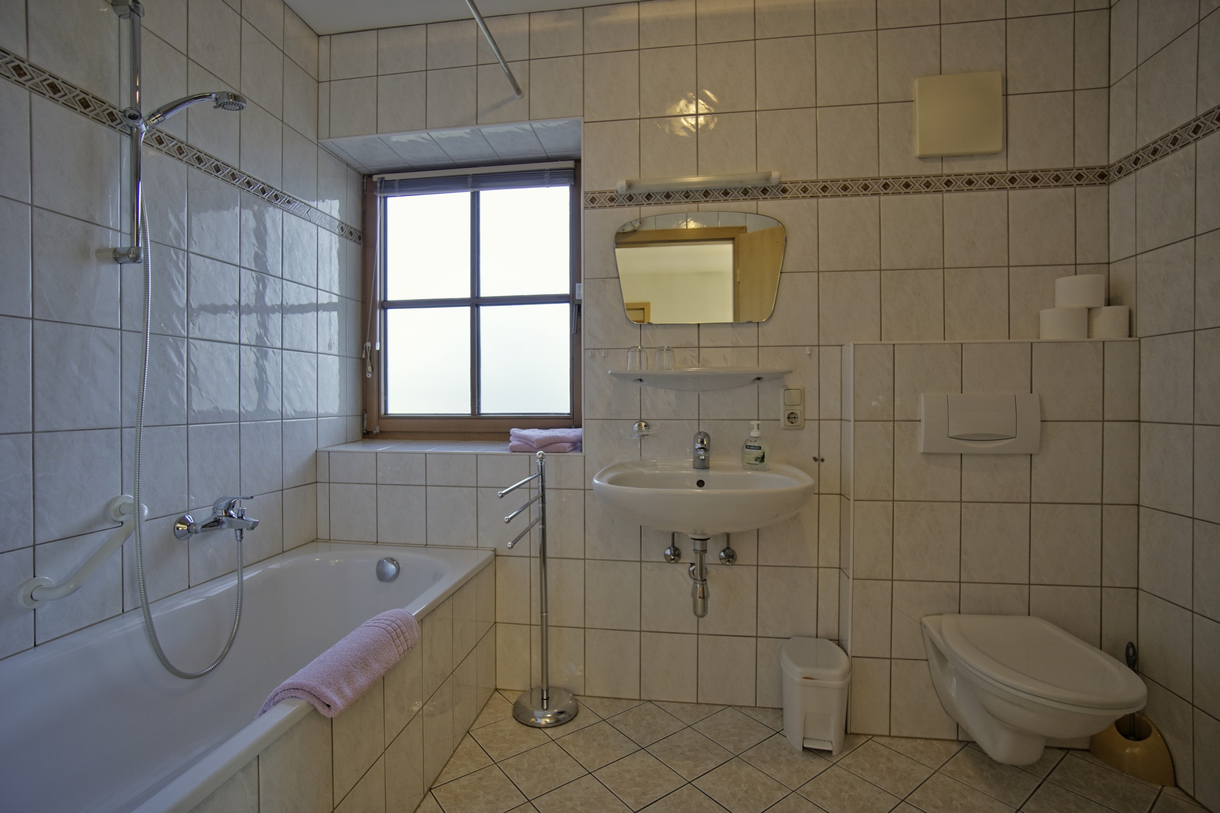 Badezimmer gefliest mit Badewanne und Fenster